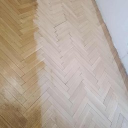 Phu Erwin Franek - Parkiet w jodełkę częściowo odnowiony, z widoczną różnicą w kolorze drewna po zabiegu. Szlifierka do parkietu w rogu kadru. Widok z góry.