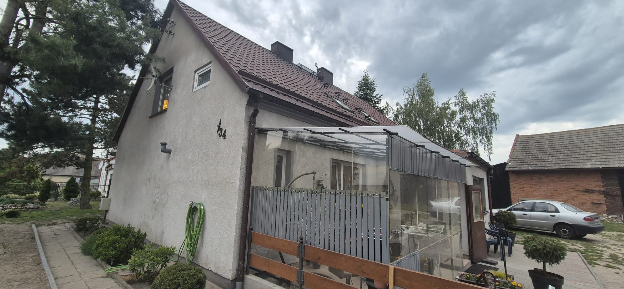 Dom jednorodzinny z dobudowaną oszkloną werandą, widok z zewnątrz. Na ścianie numer domu '134'.