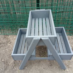 Firma Usługowo Produkcyjna - Drewniana, szara konstrukcja z trzema skrzynkami na rośliny, ustawiona na ziemi, z zieloną siatką w tle. Widok z góry, prezentujący detale wykonania i kolorystykę.