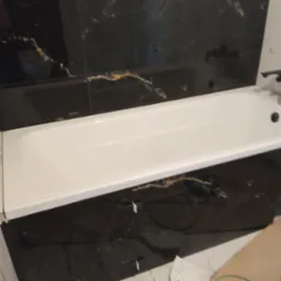 Biała wanna w łazience z czarnymi płytkami imitującymi marmur. Widoczne fugi i fragment podłogi. Ujęcie z góry, podkreślające kontrast kolorów i faktur.