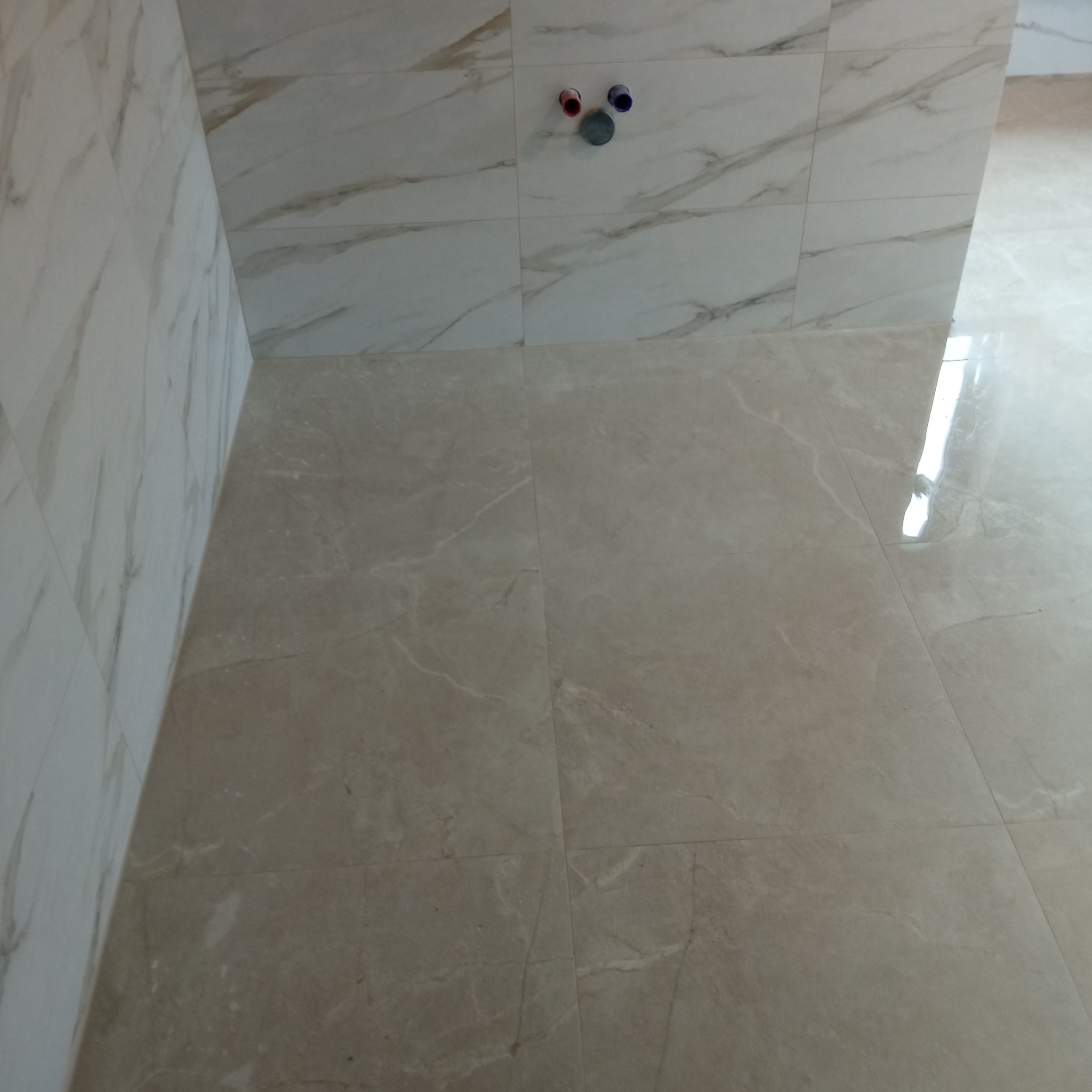 Wykończona łazienka w Witaszycach z beżowymi płytkami imitującymi marmur na podłodze i ścianach, widoczne przyłącza wodne. Jasne, nowoczesne wnętrze.