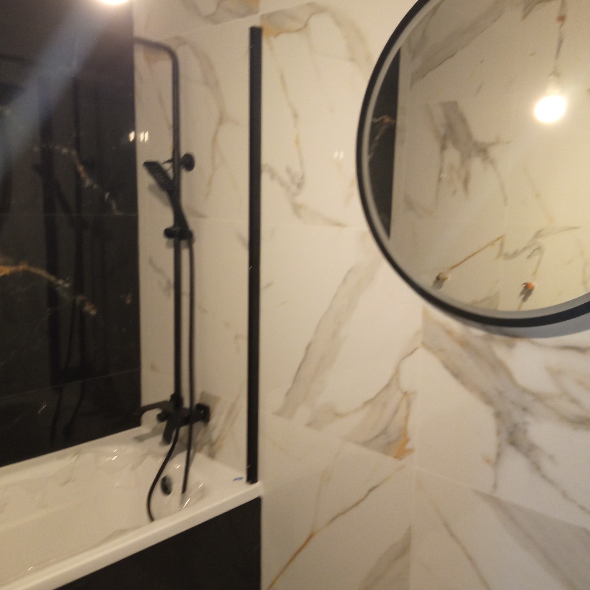 Wykończona łazienka z czarno-białymi marmurowymi płytkami, czarną armaturą i okrągłym lustrem. Nowoczesny design.