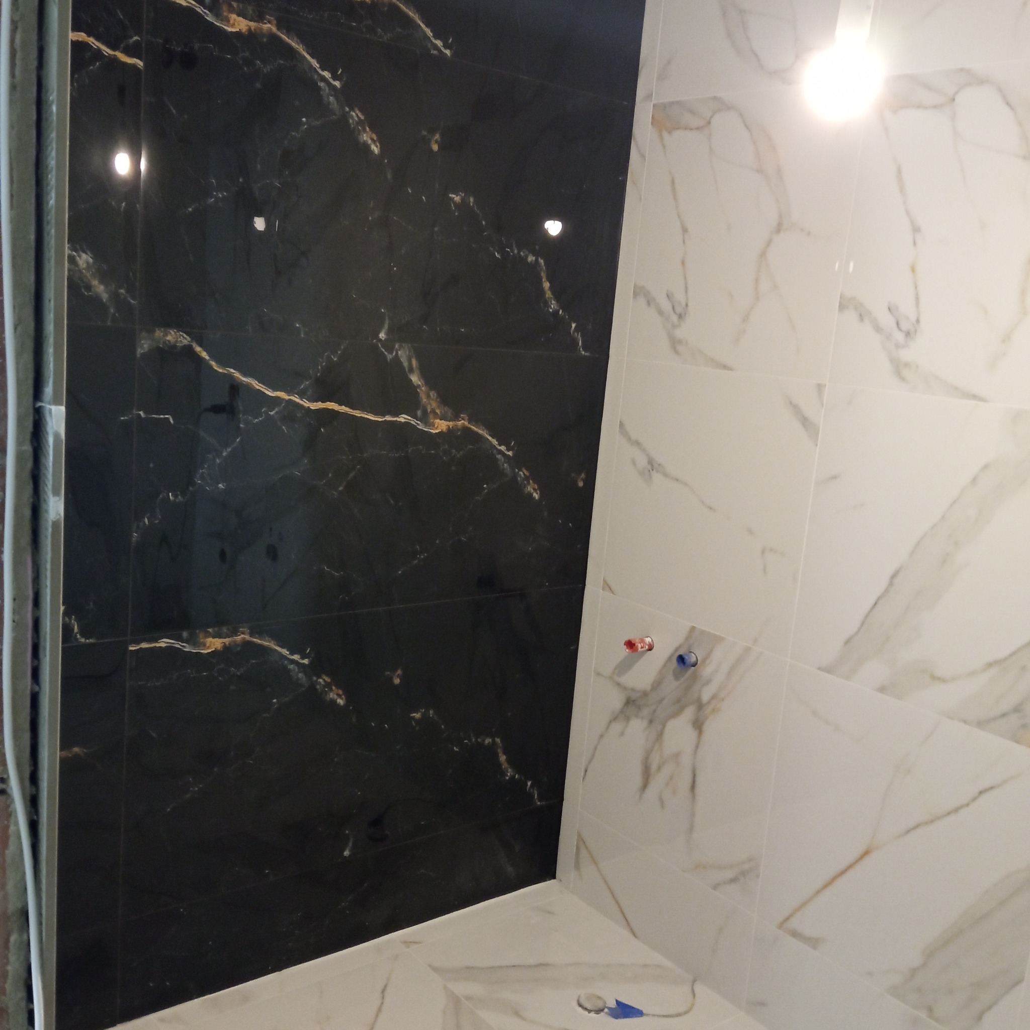 Ukończona łazienka z czarno-białymi płytkami imitującymi marmur. Widoczne przyłącza wodne i fragment instalacji. Nowoczesny design.