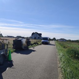ŻUK Maciej Żukowski - Przewiert sterowany Vermeer na przyczepie, wykop i bus na drodze wiejskiej, błękitne niebo. Sprzęt do instalacji podziemnych w trakcie pracy.
