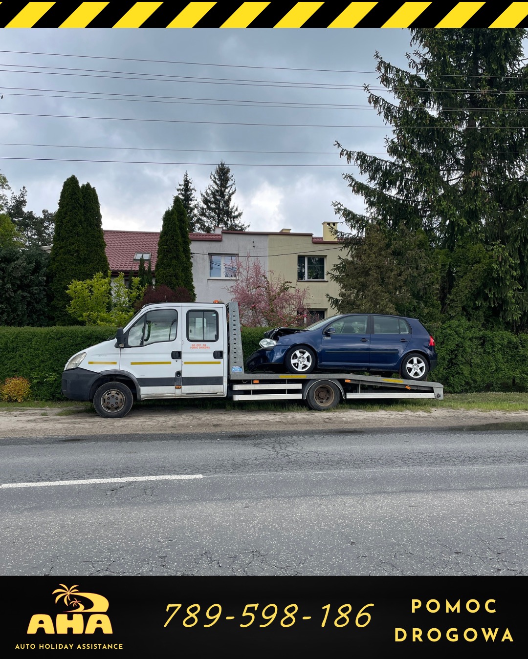 Laweta z uszkodzonym, granatowym Volkswagenem Golf na platformie, zaparkowana na poboczu drogi. W tle domy i drzewa. Widoczny numer telefonu.