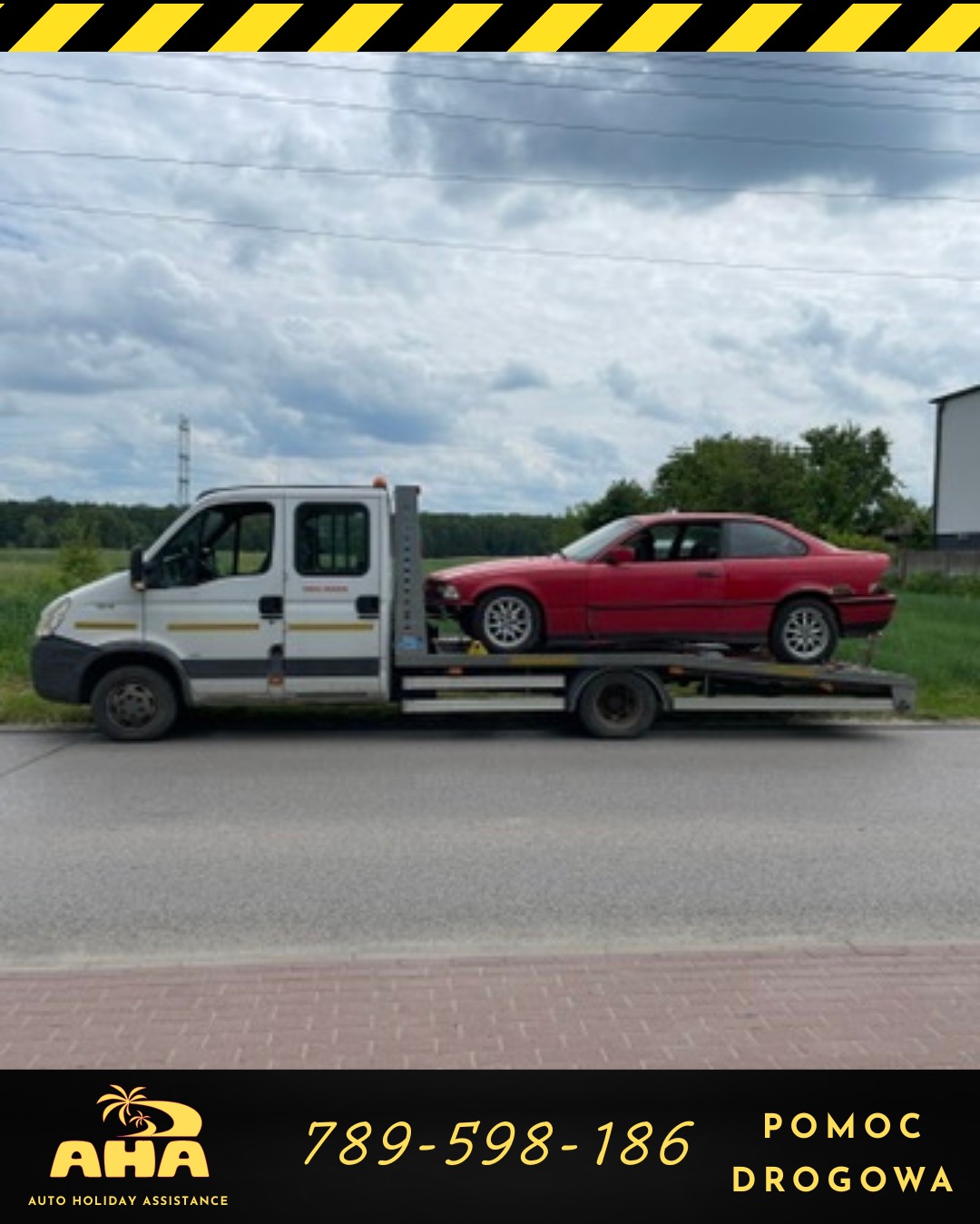 Biała laweta z czerwonym autem osobowym na platformie, widok z boku na drodze. Słoneczny dzień. AHA Auto Holiday Assistance.