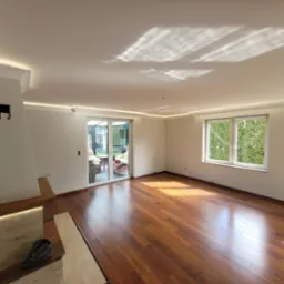 Jasne, przestronne wnętrze po remoncie: parkiet z egzotycznego drewna, białe ściany z listwami LED pod sufitem, duże okno z widokiem na zieleń, kominek z podświetleniem.