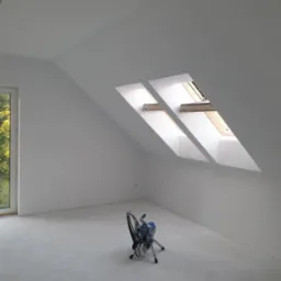 Białe poddasze po malowaniu natryskowym. Widoczne okna dachowe i urządzenie do malowania.