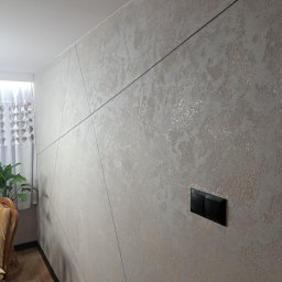 F.H.U TOBMAL TOBIASZ LASOŃ - Dekoracyjna ściana z fakturą w odcieniach beżu, przecięta czarnymi, ukośnymi liniami. Widoczny fragment okna z zasłoną i włącznik światła.