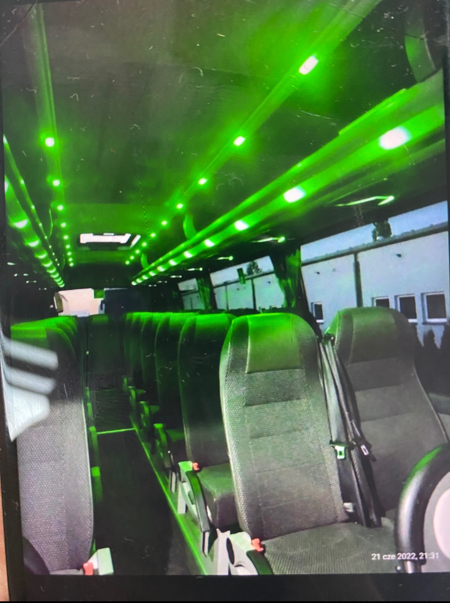 Wnętrze busa z zielonym oświetleniem LED. Widoczne rzędy foteli z pasami bezpieczeństwa i oknami. Nietypowe oświetlenie wnętrza pojazdu do transportu osób.