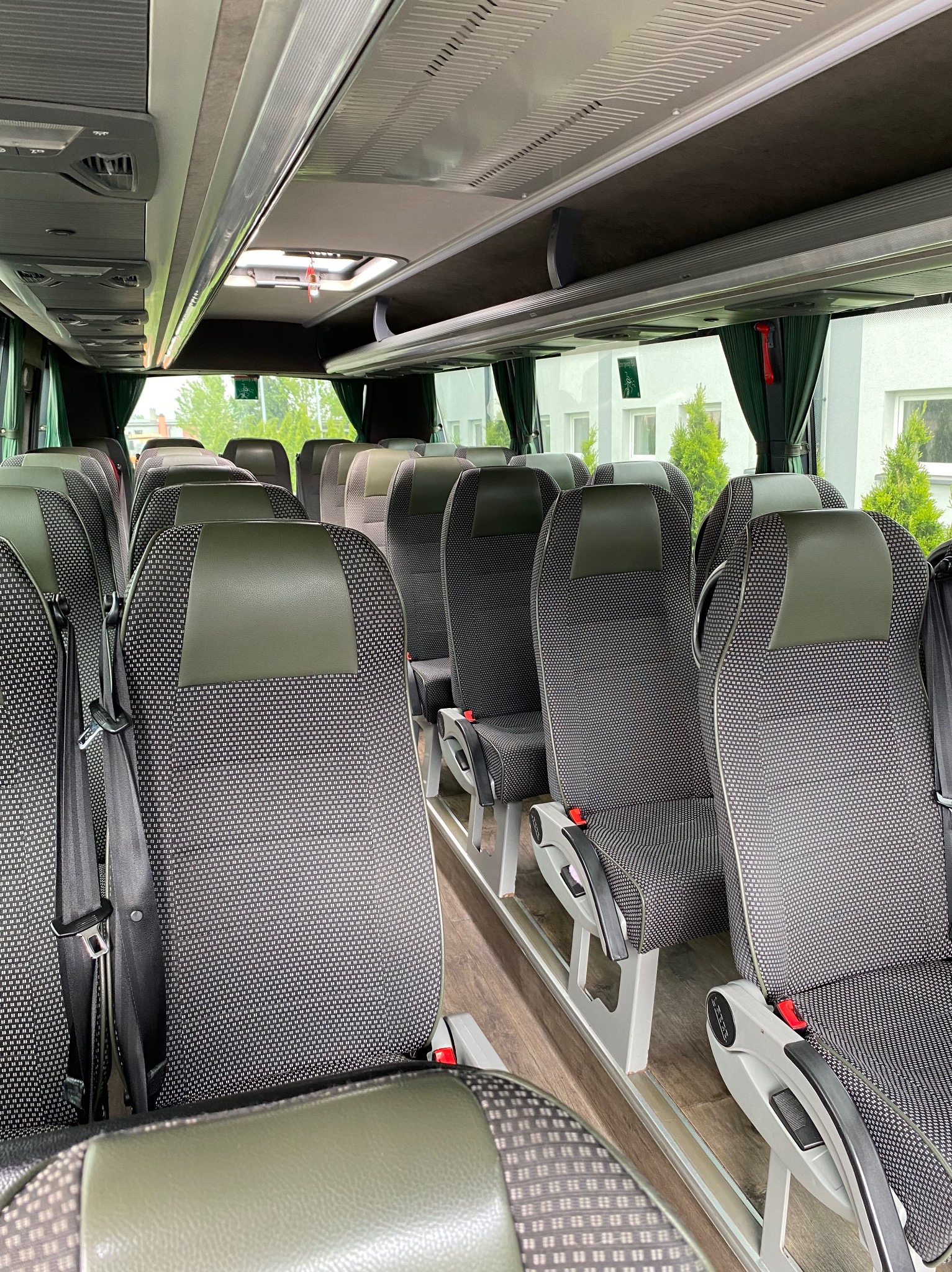Wnętrze autobusu z fotelami w tonacji szaro-zielonej, widok na przejście między rzędami siedzeń, Dąbrowa Górnicza. Czyste i zadbane wnętrze pojazdu.
