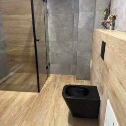 Nowoczesna łazienka – montaż czarnej ceramiki, kabina walk-in, połączenie płytek drewnopodobnych i betonowych. Precyzyjne wykonanie i nowoczesny styl.