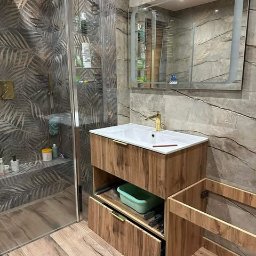 Stylowa łazienka z efektem kamienia i drewna – nowoczesna kabina walk-in, złota armatura, dekoracyjna ściana z roślinnym motywem. Precyzyjne i eleganckie wykończenie.