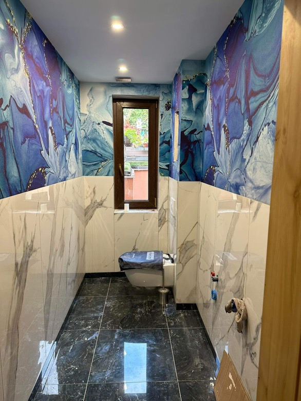 Nowoczesna łazienka po remoncie: marmurowe płytki do połowy ściany, artystyczna tapeta z motywem akwareli powyżej, czarny gres na podłodze, okno.