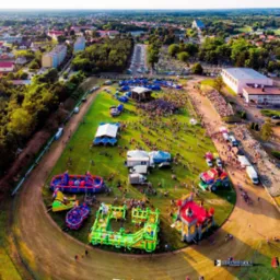 Widok z lotu ptaka na plenerową imprezę z dmuchańcami, sceną i tłumem ludzi. W tle zabudowa miejska i zieleń. Słoneczny dzień.