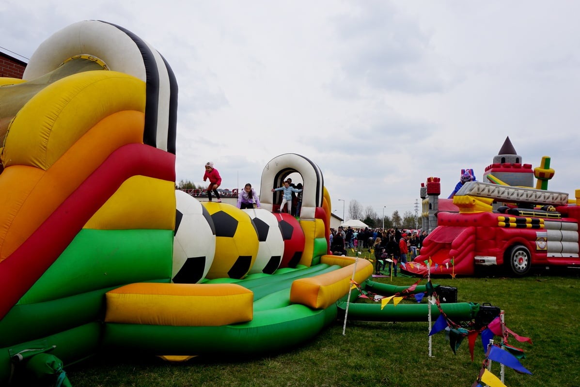 Kolorowy dmuchany plac zabaw z motywem piłki nożnej i wozem strażackim. Dzieci bawią się na dmuchańcach, w tle widoczny tłum ludzi.