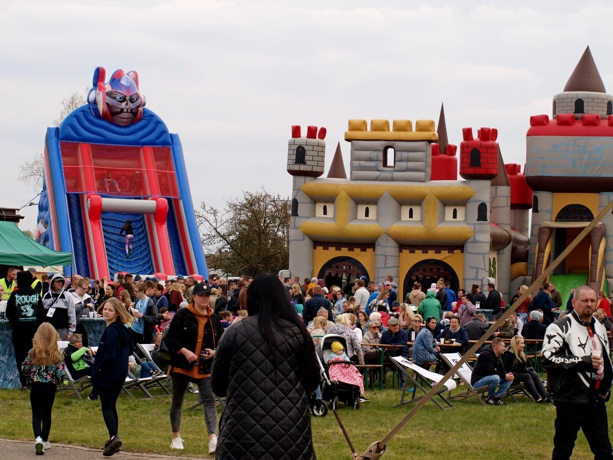 Plenerowa impreza z dmuchanymi zamkami i zjeżdżalnią dla dzieci, tłum ludzi, stoliki piknikowe. Atrakcje w parku, zabawa dla najmłodszych.
