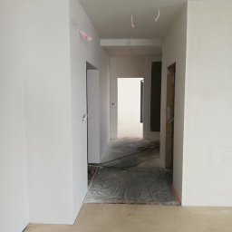 Złota rączka - Wnętrze w trakcie prac: białe ściany po świeżym malowaniu, zabezpieczona podłoga, widoczne przejścia do kolejnych pomieszczeń. Minimalistyczny efekt końcowy.