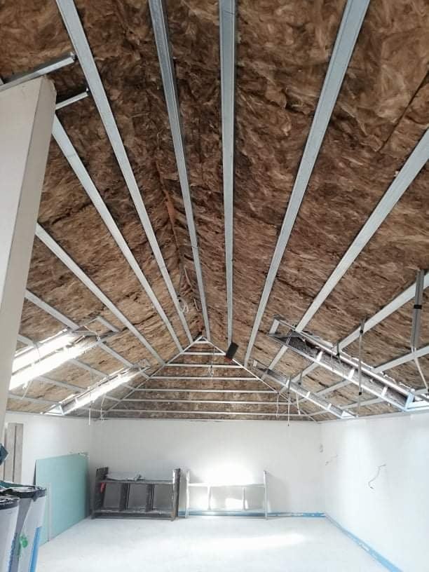 Izolacja poddasza wełną mineralną z konstrukcją metalową, widok od wewnątrz. Świeżo otynkowane ściany i przygotowane płyty.