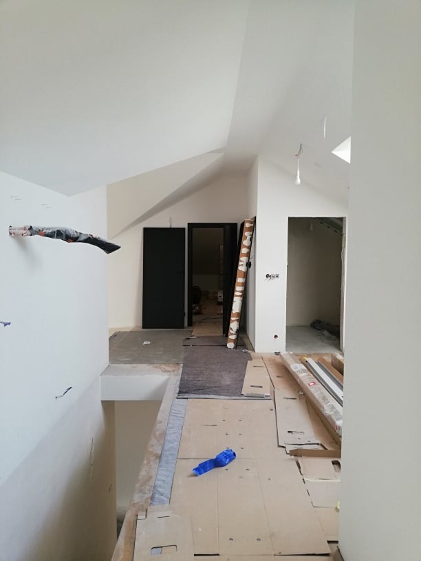 Wnętrze poddasza w trakcie prac wykończeniowych: widoczne przygotowane podłoże, surowe ściany, dwa otwory drzwiowe i zabezpieczone elementy konstrukcyjne.