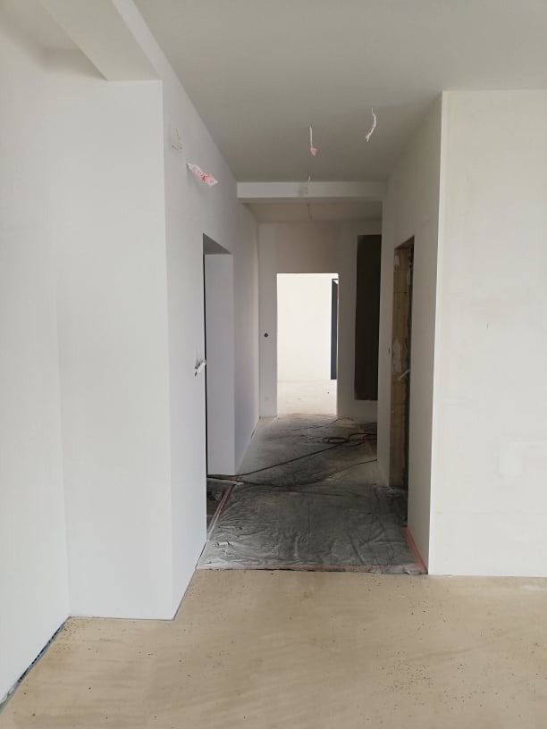 Wnętrze w trakcie prac: białe ściany po świeżym malowaniu, zabezpieczona podłoga, widoczne przejścia do kolejnych pomieszczeń. Minimalistyczny efekt końcowy.