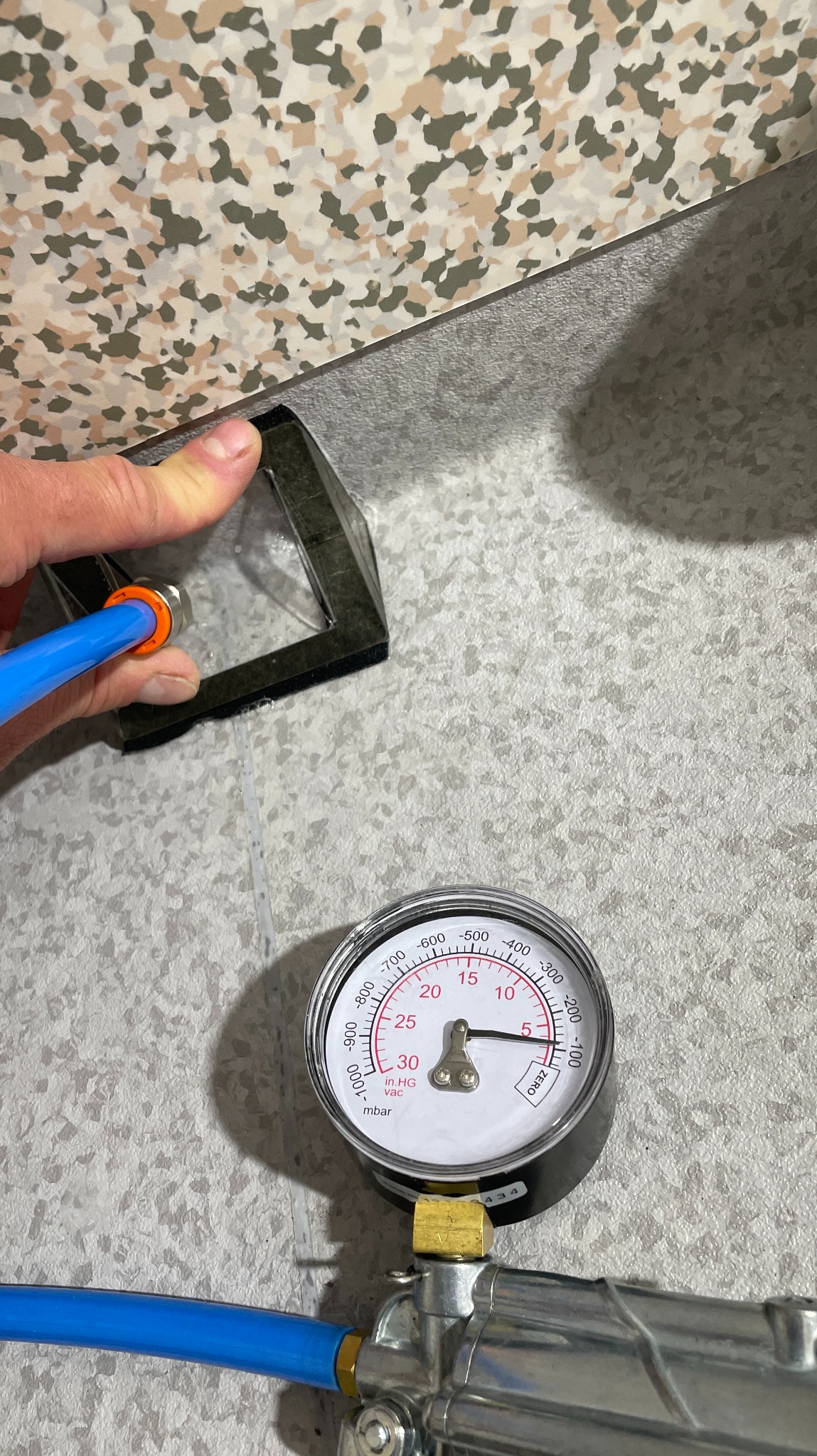 Pomiar szczelności posadzki manometrem z przyssawką, niebieski wężyk. Kontrola jakości wykonanej podłogi, wzór lastryko na podłodze. Detal z bliska.