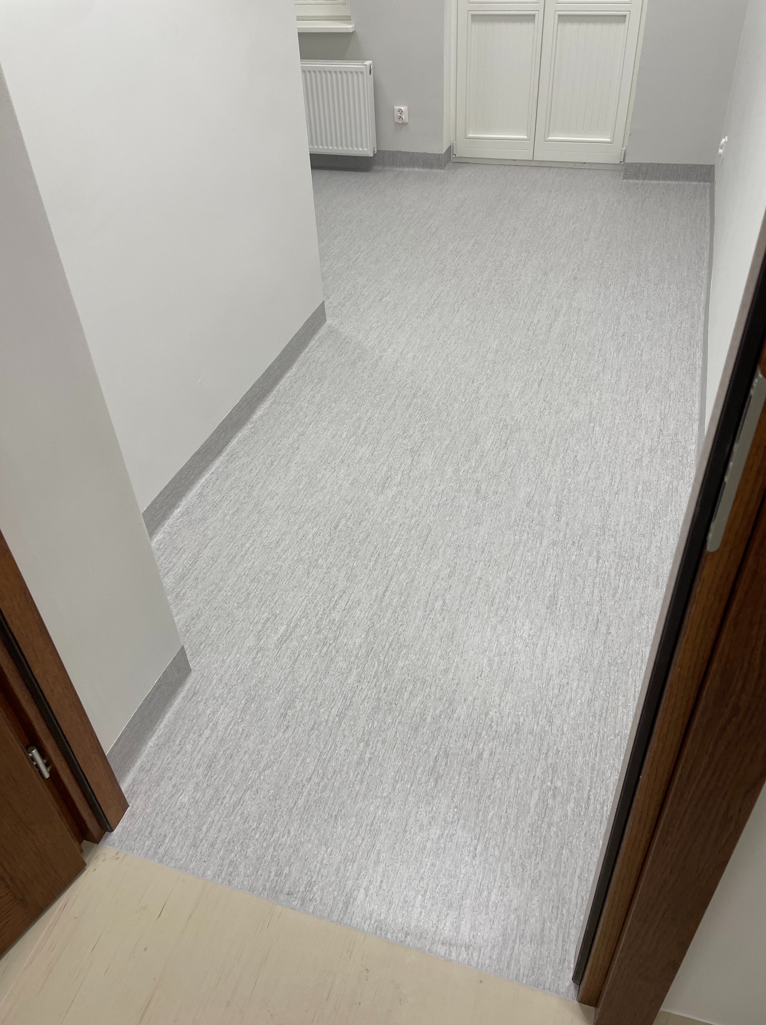 Jasnoszara, wzorzysta podłoga z listwami przypodłogowymi w odcieniach szarości, widok z progu drzwi w Koronowie. W tle białe drzwi i grzejnik.