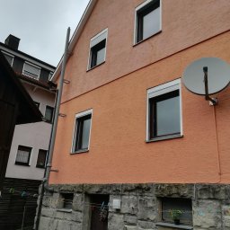 Pro Window System - Dwukondygnacyjny dom z oknami PCV z roletami zewnętrznymi, anteną satelitarną i rynną. Dolna część budynku wykończona kamieniem.