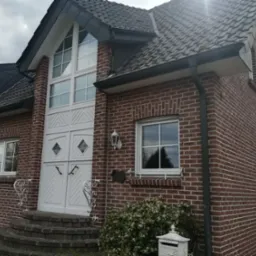 Dwuskrzydłowe, białe drzwi zewnętrzne z romboidalnymi przeszkleniami i oknem nadświetlnym w domu z czerwonej cegły. Dekoracyjne, białe balustrady.