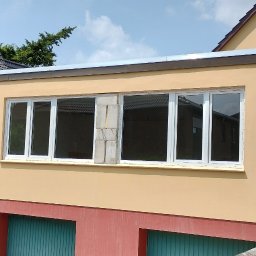 Pro Window System - Montaż okien PCV w budynku z żółtą elewacją. Widoczne okna z białymi ramami, z jednym oknem w trakcie montażu. Częściowo widoczne stare okno.