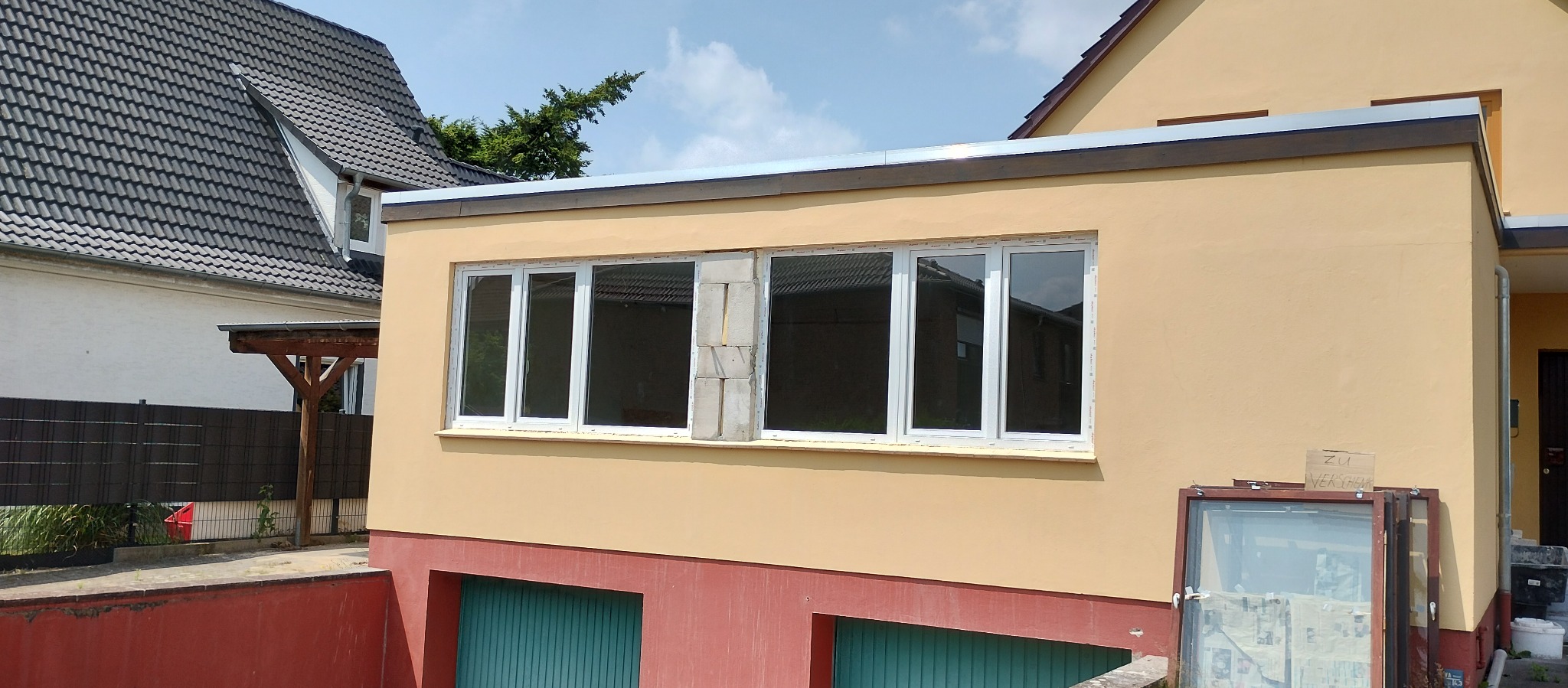 Montaż okien PCV w budynku z żółtą elewacją. Widoczne okna z białymi ramami, z jednym oknem w trakcie montażu. Częściowo widoczne stare okno.