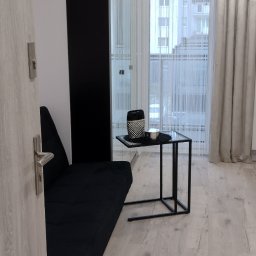 Grzegorz Jaszczuk - Nowoczesny salon w Rosanowie: czarna sofa, szklany stolik i jasna podłoga. Minimalistyczny design z widokiem na okno i firany.