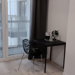 Grzegorz Jaszczuk - Jasne panele podłogowe, czarne krzesło z ażurowym oparciem i biurko z globusem w minimalistycznym, nowocześnie urządzonym pokoju z balkonem.