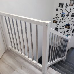 ZAB-DEKOR Arkadiusz Zabdyr - Biała balustrada schodowa z metalowymi, pionowymi prętami, widok z góry, na ścianie dekoracja w formie drzewa z ramkami na zdjęcia.