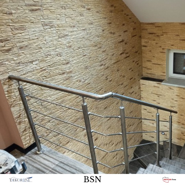 Metalowa poręcz schodowa z poziomymi elementami, na tle ściany z dekoracyjną okładziną kamienną. Widoczne schody z szarej płytki.