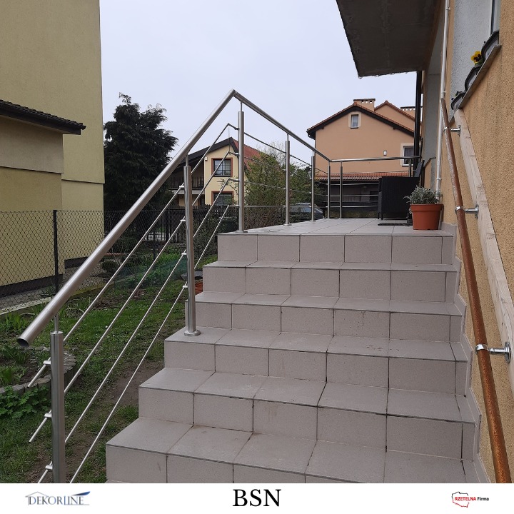Zewnętrzne schody z szarych płytek prowadzą na taras. Metalowa, nowoczesna barierka ze stali nierdzewnej z linkami zabezpiecza schody i taras.