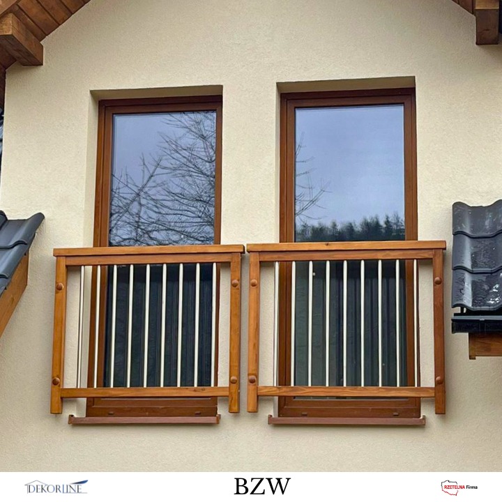 Dwa drewniane balkoniki okienne z białymi, pionowymi prętami, zamontowane na elewacji budynku. Widoczne brązowe ramy okienne i fragment dachu.
