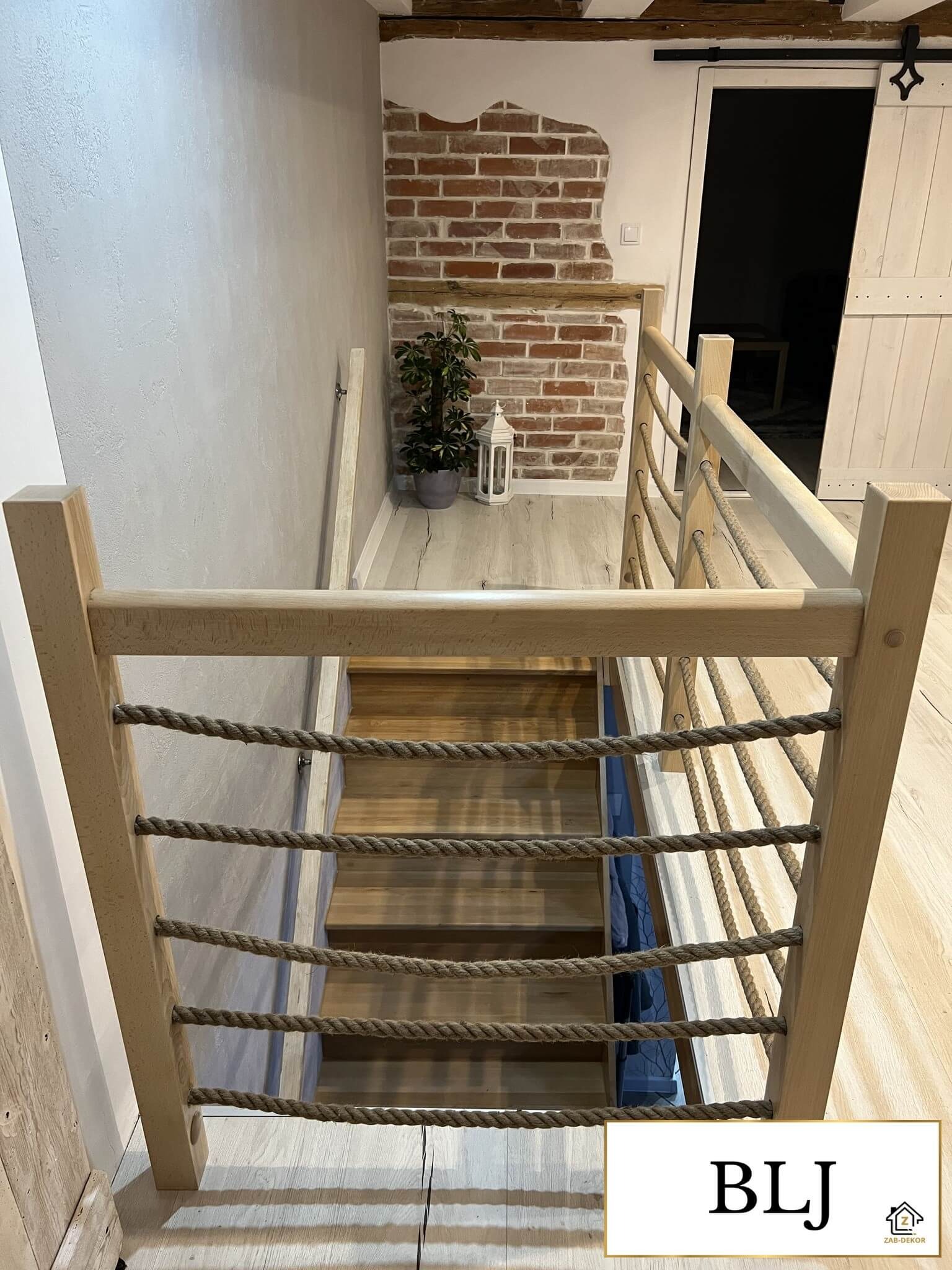 Jasne drewniane schody z oryginalną balustradą z lin, widok z góry, ceglana ściana w tle. Element wystroju wnętrza w stylu rustykalnym.