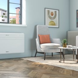 Klimatyzacja Monoblok - Biały klimatyzator ścienny Unico w nowoczesnym salonie z szarą sofą, fotelem i dywanem. Widok na okno z roślinami i budynkami w tle. Minimalistyczny design.