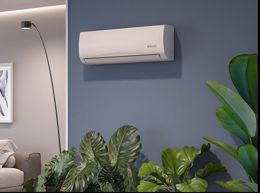 Biała klimatyzacja ścienna Olympia Splendid w nowoczesnym wnętrzu z szarą ścianą, lampą łukową i zielonymi roślinami. Elegancki design urządzenia.