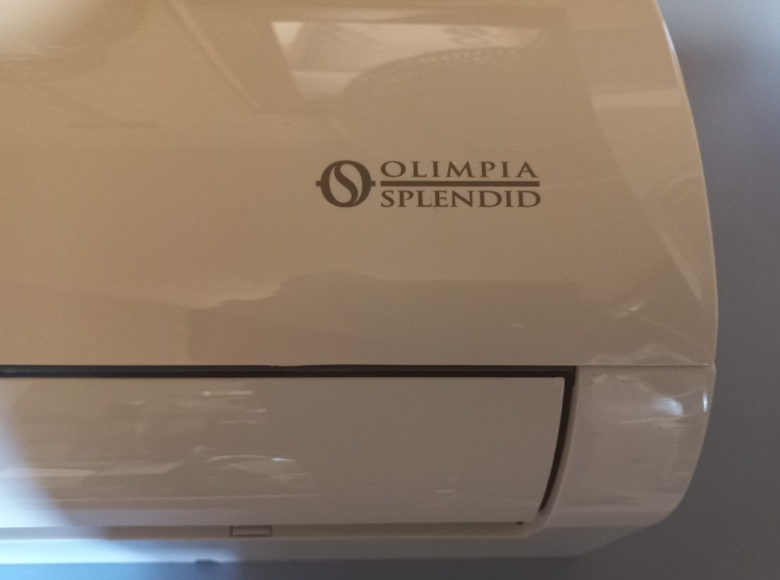 Klimatyzator marki Olimpia Splendid, kremowy odcień obudowy. Widoczne logo producenta. Urządzenie zamontowane na ścianie.