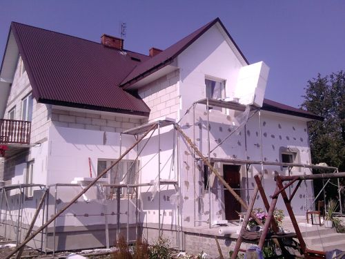 Dom jednorodzinny w trakcie ocieplania styropianem, widoczne rusztowania i fragmenty niezabezpieczonej elewacji.