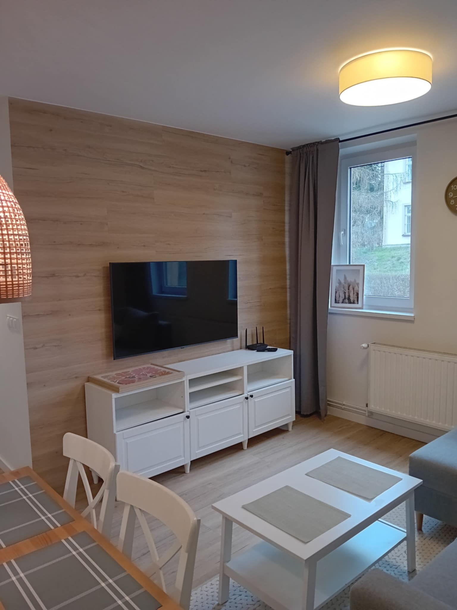 Wykończony salon w Krosno z drewnianą ścianą za telewizorem, białą komodą i stolikiem kawowym, szare zasłony w oknie.