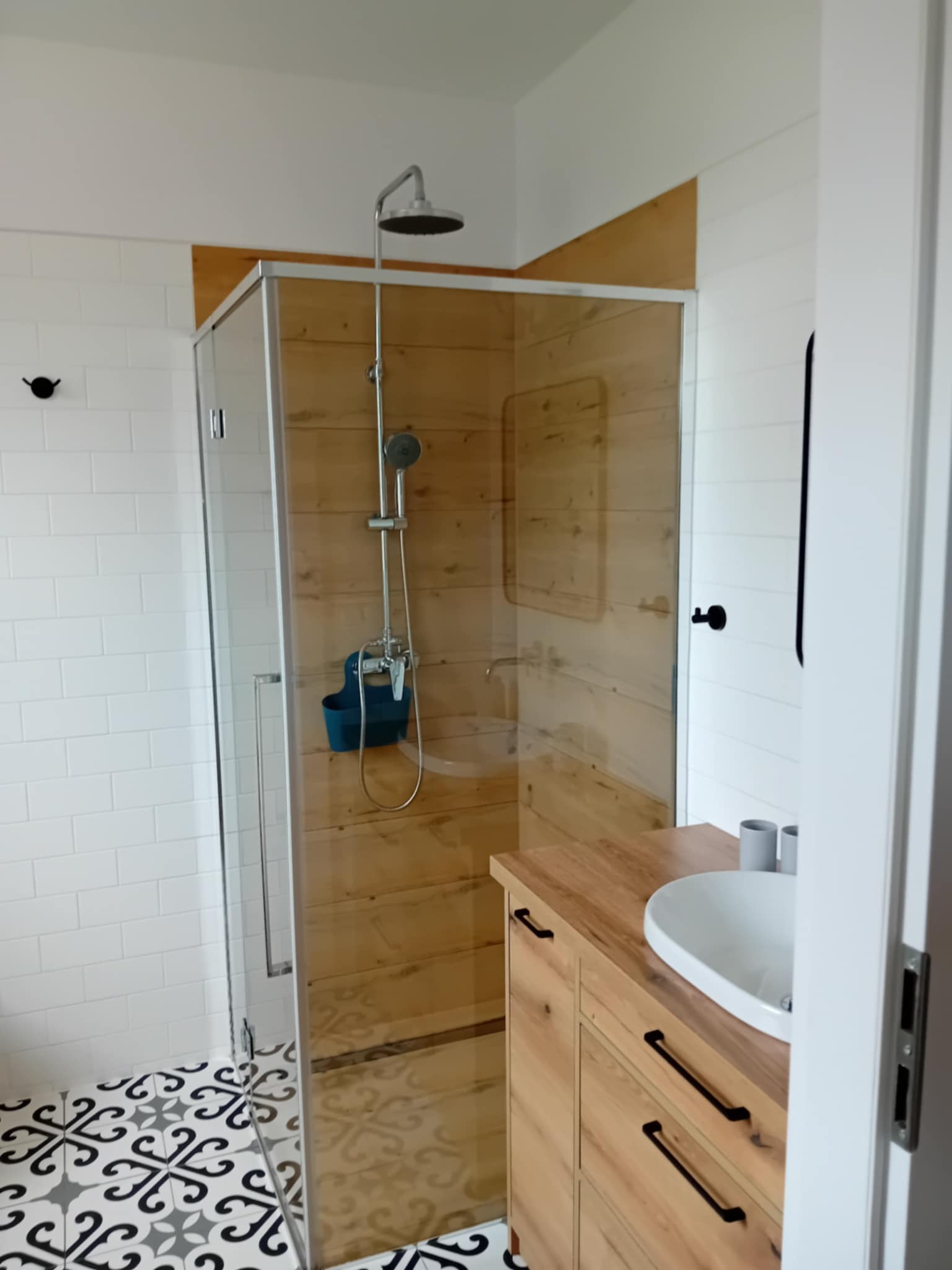Nowoczesna łazienka z kabiną prysznicową typu walk-in, wykończoną drewnem, białą ceramiką i wzorzystą podłogą. Minimalistyczny design.