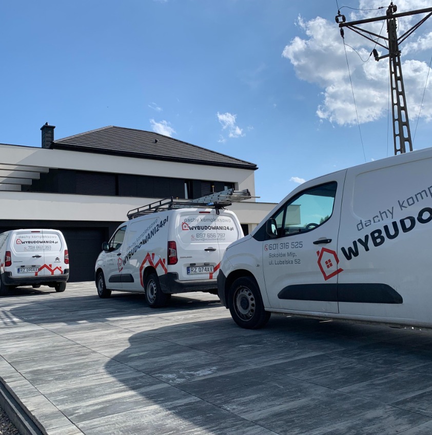 Trzy białe busy firmy dekarskiej z logo na tle nowoczesnego domu z ciemnym dachem i błękitnego nieba. Jeden z busów ma drabinę na dachu. Kostka brukowa na podjeździe.