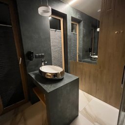 4M Marcin Marcinkowski - Nowoczesna łazienka z umywalką nablatową w kolorze złota, szare ściany z fakturą i oświetlenie LED. Minimalistyczny design i eleganckie wykończenie.