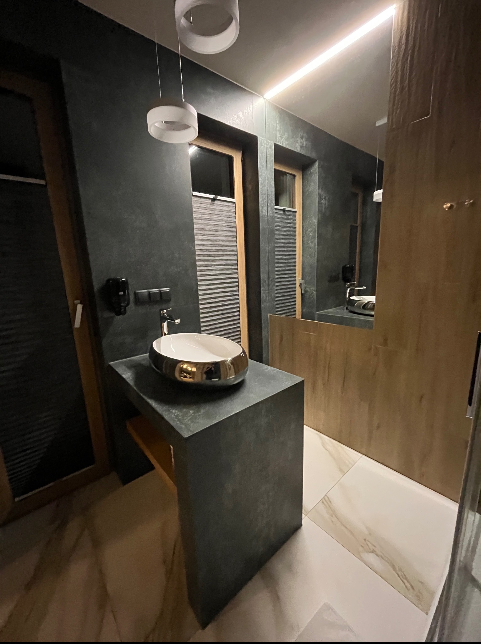 Nowoczesna łazienka z umywalką nablatową w kolorze złota, szare ściany z fakturą i oświetlenie LED. Minimalistyczny design i eleganckie wykończenie.