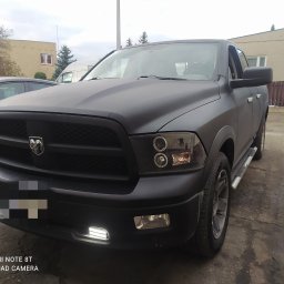 Vernus Auto Expert - Czarny Dodge Ram po tuningu z ledowymi światłami dziennymi, zaparkowany przed budynkiem. Matowa karoseria, widoczne detale grilla i opon.