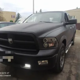 Czarny Dodge Ram po tuningu z ledowymi światłami dziennymi, zaparkowany przed budynkiem. Matowa karoseria, widoczne detale grilla i opon.
