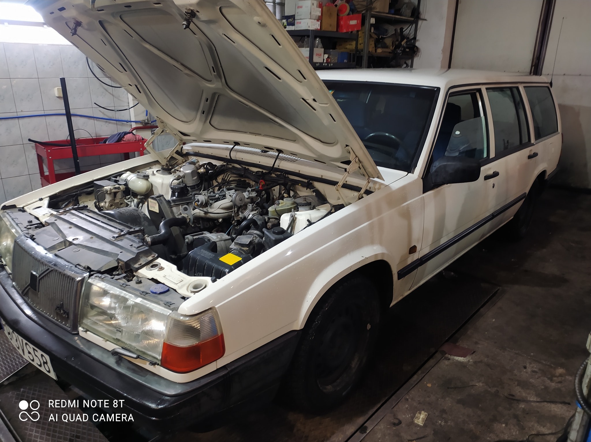 Białe Volvo kombi z otwartą maską silnika w warsztacie w Skórzewie. Widoczne elementy silnika i wnętrze warsztatu.